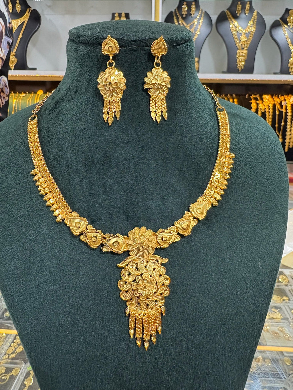 Gold plated floral necklace and earring set displayed on a dark green jewellery bust