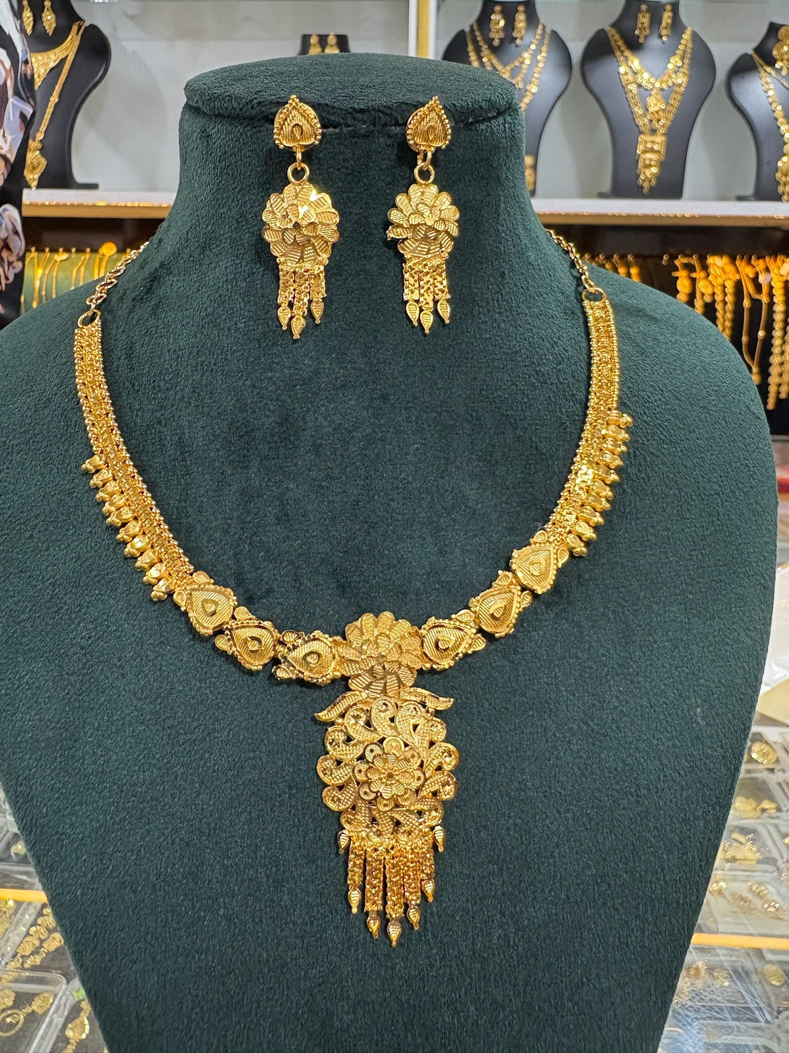 Gold plated floral necklace and earring set displayed on a dark green jewellery bust